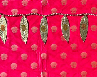 May include: A gold leaf garland with a beaded string, hanging on a red fabric background with a repeating pattern.