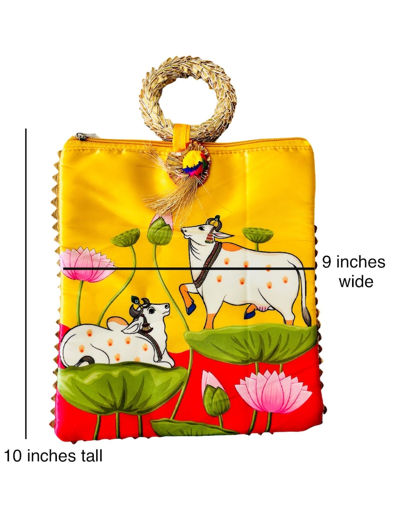 Pode incluir: Uma bolsa amarela, com 25 cm de altura e 23 cm de largura, com uma al&ccedil;a tecida. A bolsa apresenta uma pintura de duas vacas brancas com manchas marrons, flores de l&oacute;tus e folhas de nen&uacute;far verdes. A bolsa tem uma borda vermelha.