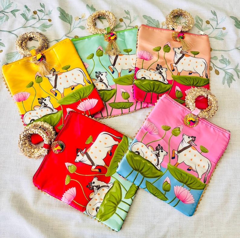 Pode incluir: Uma cole&ccedil;&atilde;o de bolsas de tecido quadradas e coloridas. Cada bolsa apresenta um design pintado &agrave; m&atilde;o de uma vaca branca com manchas marrons, flores de l&oacute;tus e folhas verdes. As bolsas est&atilde;o em tons de amarelo, vermelho, rosa, verde e p&ecirc;ssego.