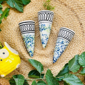 May include: Three white ceramic wall planters with black geometric designs and blue and green marbling. The planters are cone-shaped and have a pointed bottom.