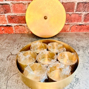 May include: A round brass spice box with a lid. The box has seven individual compartments for storing spices. The lid has a decorative design.