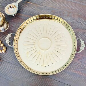 May include: A gold serving tray with a decorative floral design and two handles. The tray is on a wooden surface.