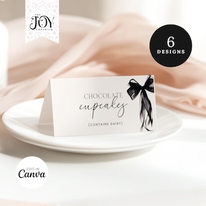 Può includere: Biglietto da tavolo bianco con la scritta "Chocolate cupcakes" e un'illustrazione di fiocco nero. La carta include anche la scritta "(CONTIENE LATTE)" ed è su un piatto bianco. Un cerchio nero con "6 DESIGNS" è sullo sfondo.