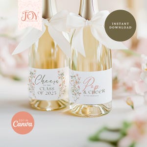 May include: Two champagne bottles with white labels featuring floral designs and text. One label reads "Cheers to the Class of 2025," and the other says "Pop & Cheer to the Graduate." Each bottle is adorned with a white ribbon.