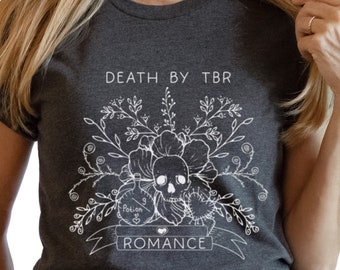 May include: A dark gray t-shirt with a white graphic design of a skull with flowers and a banner that reads "Death by TBR Romance".