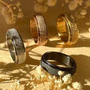Könnte beinhalten: Vier drehbare Ringe mit glitzerndem Finish. Die Ringe sind in Silber, Gold, Roségold und Schwarz.