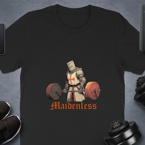 Könnte beinhalten: Schwarzes T-Shirt mit einer Grafik eines Ritters, der Gewichte hebt, und dem Wort "Maidenless" in orangefarbener Schrift. Der Ritter trägt einen Helm und eine Rüstung mit rotem Kreuz. Weitere Artikel sind Telefon, Uhr und Schuhe. Das T-Shirt ist aus Baumwolle.