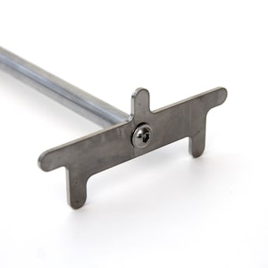 May include: A silver metal tool with a long handle and a T-shaped head. The head has two prongs on either side of a screw.