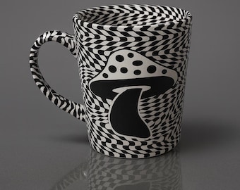 May include: A ceramic mug with a black and white wavy pattern and a black mushroom graphic. The mug has a curved handle and a glossy finish. The mushroom design is centered on the mug's front.