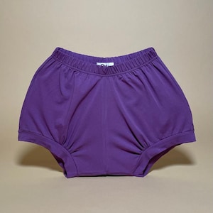 May include: Purple cotton shorts with a wide elastic waistband. The shorts have a gathered, bubble hem.