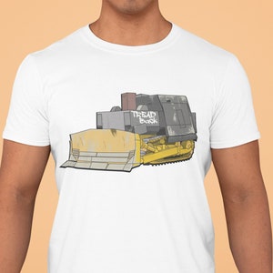 Może przedstawiać: Biała koszulka z grafiką przedstawiającą żółtą i szarą buldożerkę z napisem "TREAD BACK" na boku.