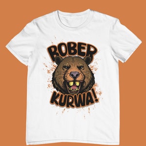 Può includere: Maglietta bianca con un castoro di cartone animato marrone con un ghigno pieno di denti e il testo "ROBER KURWA!" in arancione e nero.