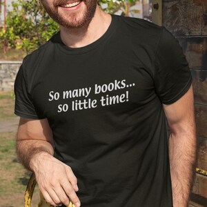 以下が含まれることがあります： 白い文字で「So many books... so little time!」と書かれた黒いTシャツ