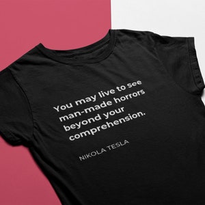 May include: Black t-shirt with a white quote that reads "You may live to see man-made horrors beyond your comprehension." The quote is attributed to Nikola Tesla.