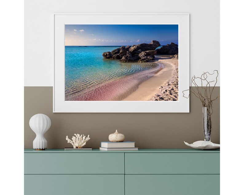 May include: A framed photograph of a beach with turquoise water, pink sand, and rocky outcrops. The sky is blue with white clouds.