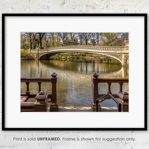 Pode incluir: Uma vista de uma ponte de pedra sobre um lago calmo em um parque. A ponte tem um design decorativo e se reflete na água. O lago é cercado por árvores e vegetação.