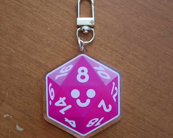 May include: Pink acrylic keychain shaped like a 20-sided die with white numbers and a smiley face on the front. The keychain has a silver metal clasp.