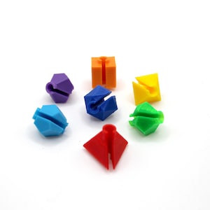 May include: A set of six colourful plastic connectors in various shapes, including a cube, pyramid, and diamond. The connectors are designed to be used with other building blocks.