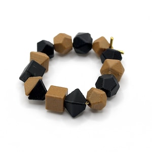 May include: A bracelet made of brown and black wooden beads. The beads are shaped like geometric diamonds and are strung together on a gold wire.