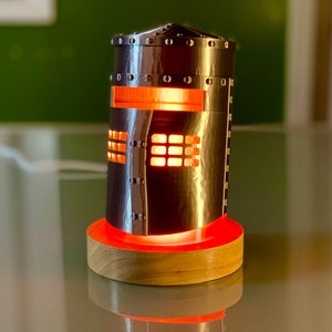 May include: A silver metal knight helmet lamp with a red light shining through the eye holes. The lamp is on a wooden base.