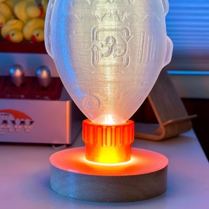 May include: A clear plastic lamp with a textured surface, shaped like a fish. The lamp has an orange base with a light inside, casting a warm glow.