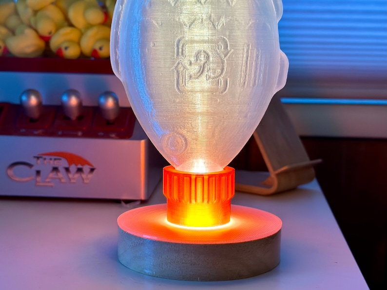 May include: A clear plastic lamp with a textured surface, shaped like a fish. The lamp has an orange base with a light inside, casting a warm glow.