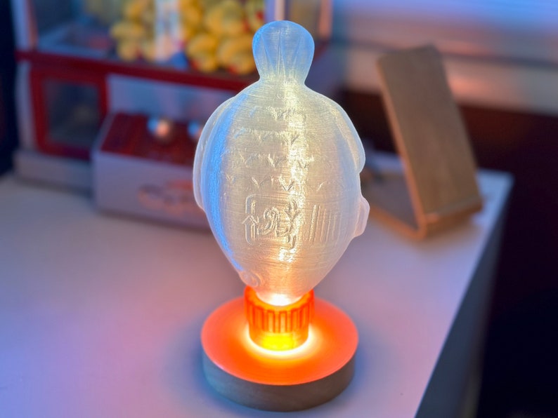 May include: A white, translucent, 3D printed turtle lamp with a warm orange glow emanating from the base. The turtle has a detailed design on its shell.