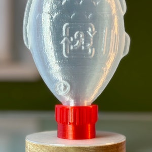 May include: A clear plastic bottle shaped like a fish with a red screw-on cap. The bottle has a recycling symbol on the side.