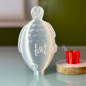 May include: A white plastic bottle with a textured surface and a recycling symbol. The bottle is sitting on a table next to a red plastic cap.