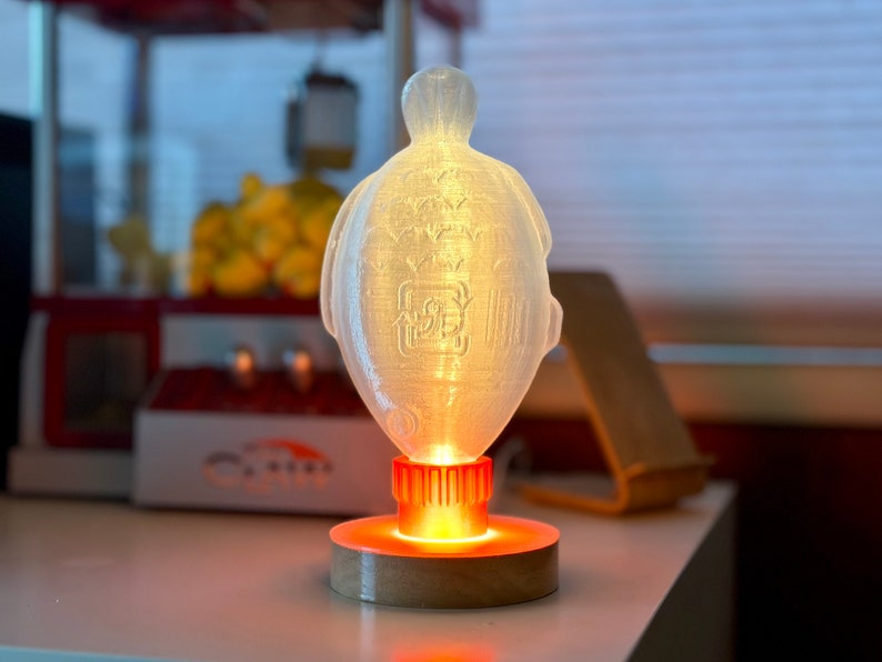 May include: A white, translucent, 3D printed lamp shaped like a turtle with a glowing orange base.