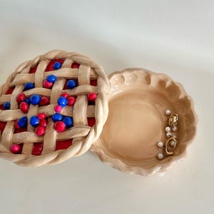 May include: A ceramic pie dish with a lid. The lid is decorated with a pie crust design and red and blue berries. The dish is empty.