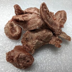 May include: A pile of brown, dried, meaty dog treats on a white surface.