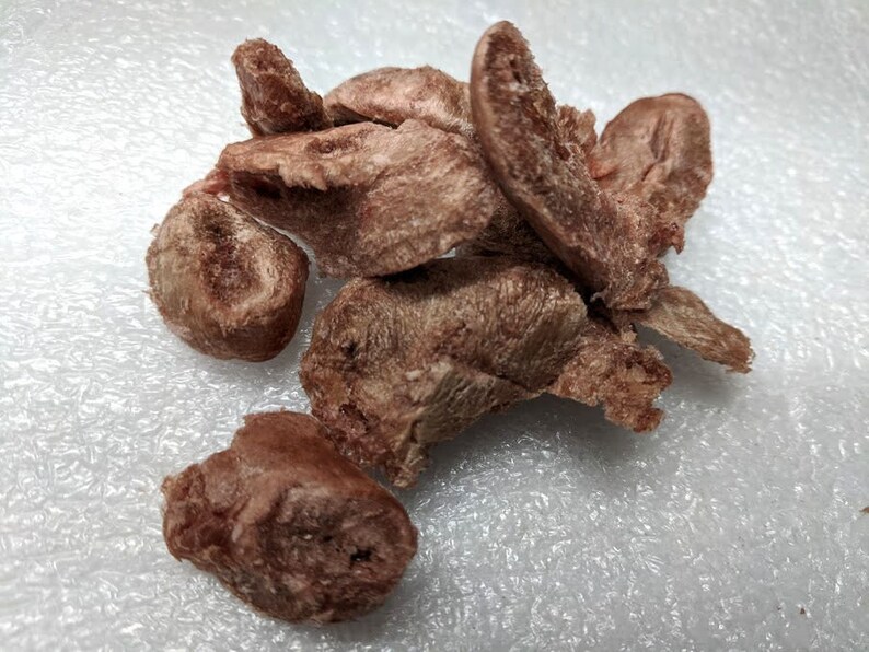 May include: A pile of brown, dried, meaty dog treats on a white surface.