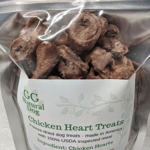 May include: A bag of freeze-dried chicken heart dog treats. The bag is white with green leaves and the text "GG Natural Dog Chicken Heart Treats" and "Freeze-dried dog treats - made in America with 100% USDA inspected meat. Ingredient: Chicken Hearts. Net weight: 2.5 oz."
