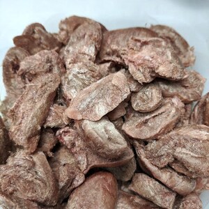May include: A close-up of a container filled with dried, shredded, light brown meat. The meat is in various shapes and sizes, and appears to be a type of jerky.