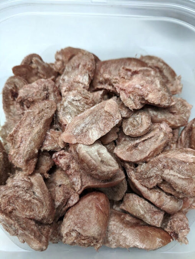 May include: A close-up of a container filled with dried, shredded, light brown meat. The meat is in various shapes and sizes, and appears to be a type of jerky.