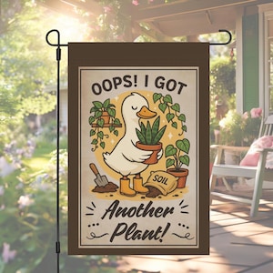 Op de afbeelding: Bruine tuin vlag met een illustratie van een eend die een potplant vasthoudt. De tekst luidt "Oops! I Got Another Plant!" in een speels lettertype. Andere planten, een schop en een zak aarde zijn ook afgebeeld.