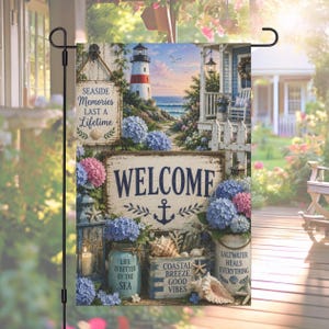 May include: A decorative garden flag featuring a coastal scene with a lighthouse, ocean, and a welcoming sign. The flag includes text that reads "Seaside Memories Last a Lifetime" and "Welcome". Blue and pink hydrangeas and seashells are also featured.