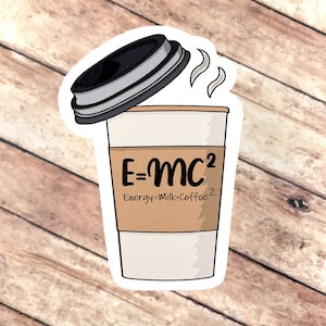 Könnte beinhalten: Ein Aufkleber mit einer Kaffeetasse mit der Aufschrift E=mc² auf der Seite. Der Text unter der Gleichung lautet „Energy=Milk•Coffee²“. Die Tasse hat einen schwarzen Deckel und Dampf steigt auf.
