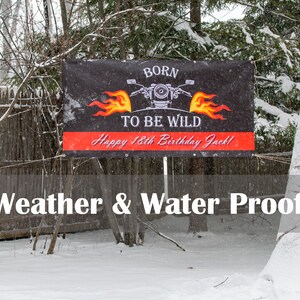 A vinyl birthday banner hung outside, between two trees. It is snowing and the trees and banner are also covered with snow. This picture shows how vinyl banners are weather and water proof.