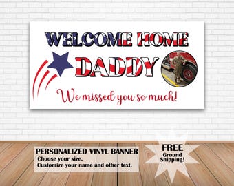 May include: A white banner with the words "WELCOME HOME DADDY" in red, white, and blue. A photo of a person in uniform is on the right. Below, it says "We missed you so much!" in red. The banner is personalized.