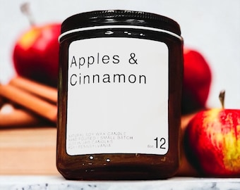 Può includere: Una candela in barattolo marrone con coperchio nero ed etichetta bianca con la scritta "Apples & Cinnamon". La candela è da 227g ed è circondata da mele rosse e bastoncini di cannella.