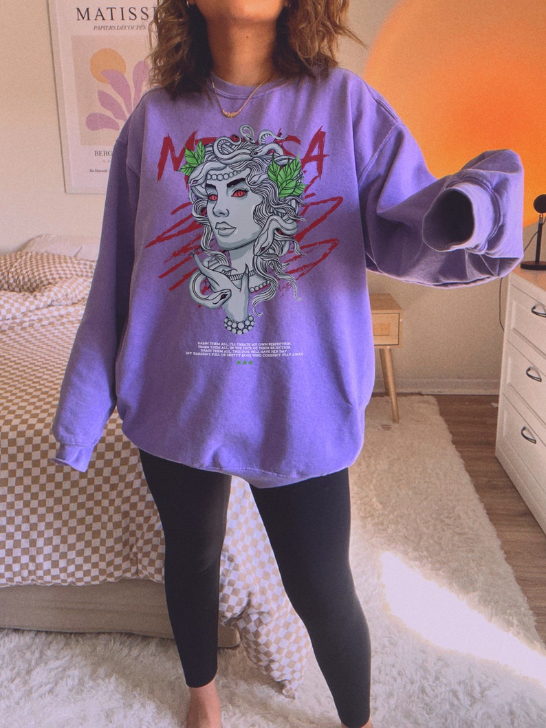 May include: Purple sweatshirt with a graphic print of a woman with snakes for hair. The graphic is in red, green, and white. The text "MEDUSA" is printed in red on the sweatshirt.