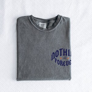 May include: A gray t-shirt with a blue graphic that says "NOTHING LASTS FOREVER" with a small orange graphic above the text.