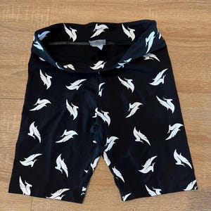 May include: Black cycling shorts featuring a white feather pattern. The shorts are made from a stretchy fabric and have a high waistband. The feather design is repeated across the shorts.