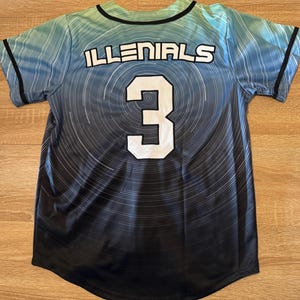 May include: A baseball jersey with the word "ILLENIALS" across the chest and the number "3" on the back. The jersey has a gradient design, transitioning from blue-green at the top to black at the bottom, with white circular lines.