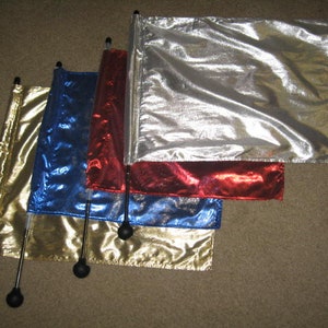 May include: Four fabric flags on black poles with black ball tips. The flags are gold, blue, red, and silver. The flags are made of a shiny, metallic fabric.