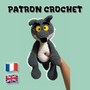 May include: A handmade crochet wolf plushie in shades of gray and white, with yellow eyes and a black nose. The text "PATRON CROCHET" is displayed above the plushie. The plushie is held against a light green background.