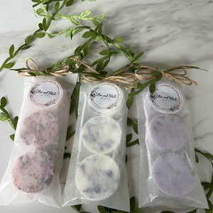 May include: Three small packages of wax melts, each containing two round wax melts. The wax melts are in different colors: pink, white, and purple. Each package has a label that says "Olive and Hatch Gifts".