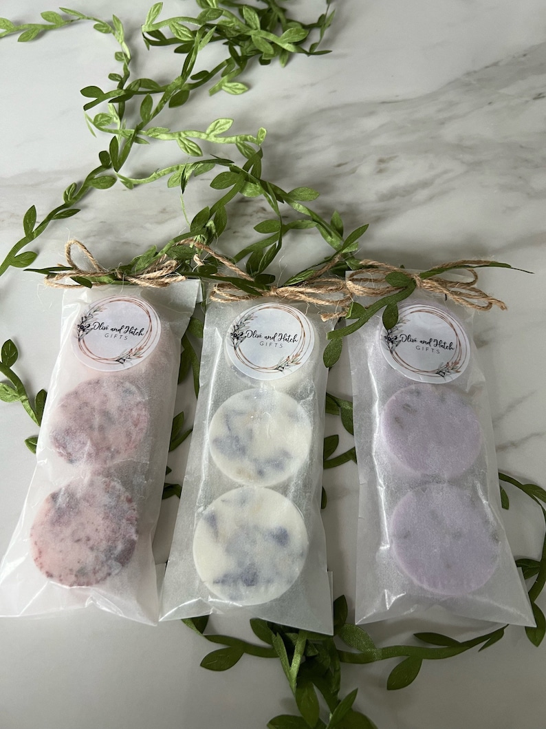 May include: Three small packages of wax melts, each containing two round wax melts. The wax melts are in different colors: pink, white, and purple. Each package has a label that says "Olive and Hatch Gifts".